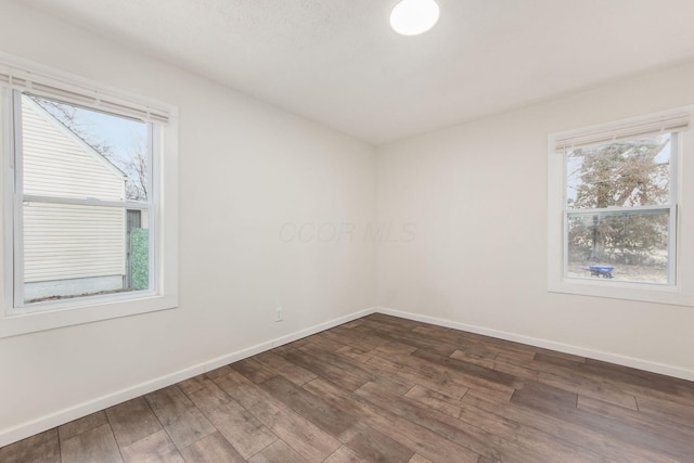 spare room featuring dark wood-style floors and baseboards