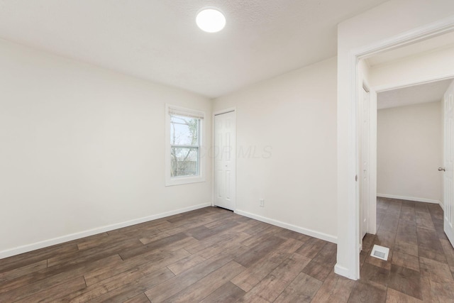 empty room featuring dark wood-style floors, visible vents, and baseboards