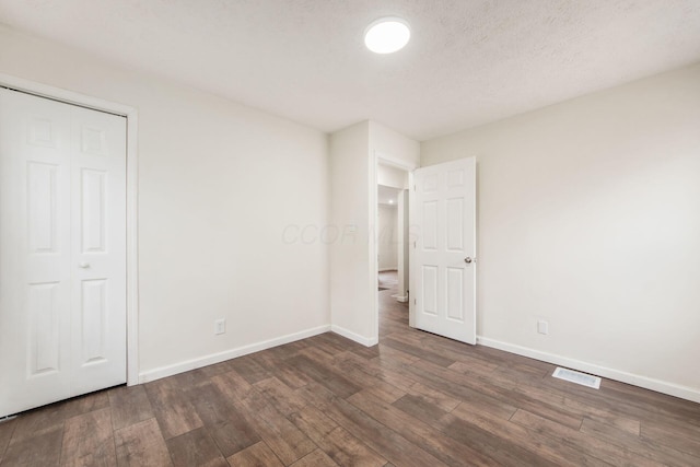 unfurnished bedroom with dark wood-type flooring, visible vents, a textured ceiling, and baseboards