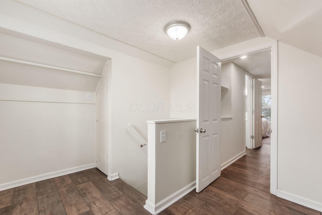 hall featuring baseboards, a textured ceiling, an upstairs landing, and wood finished floors