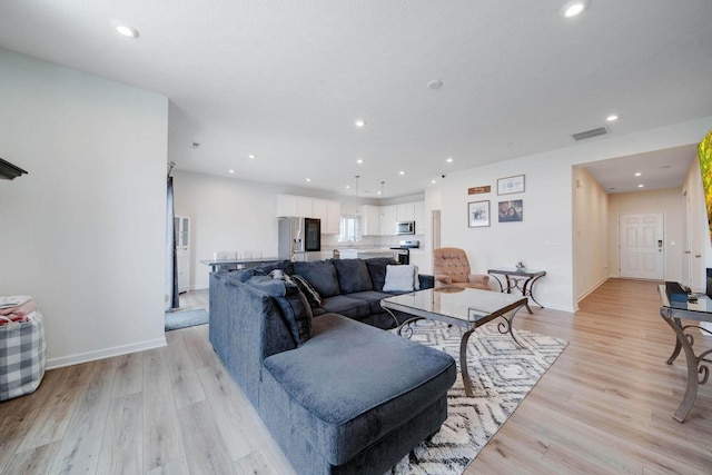 living room with light wood-type flooring, visible vents, baseboards, and recessed lighting