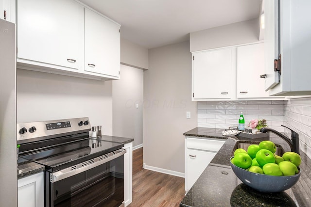 kitchen with dark stone counters, wood finished floors, stainless steel range with electric stovetop, white cabinetry, and backsplash