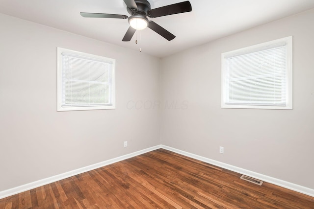 spare room with dark wood-style floors, a ceiling fan, visible vents, and baseboards