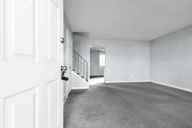 empty room featuring dark colored carpet, stairway, and baseboards