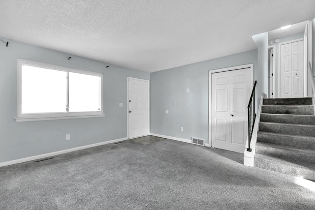 interior space featuring baseboards, visible vents, stairway, dark colored carpet, and a textured ceiling