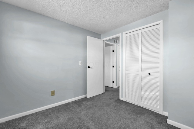 unfurnished bedroom with a closet, dark carpet, a textured ceiling, and baseboards