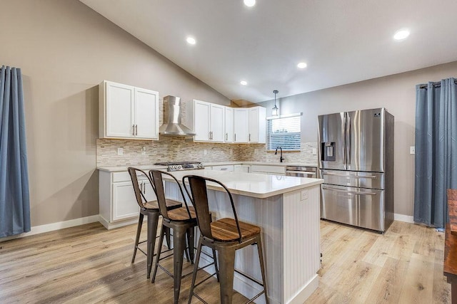 kitchen with stainless steel appliances, light countertops, white cabinetry, and wall chimney range hood