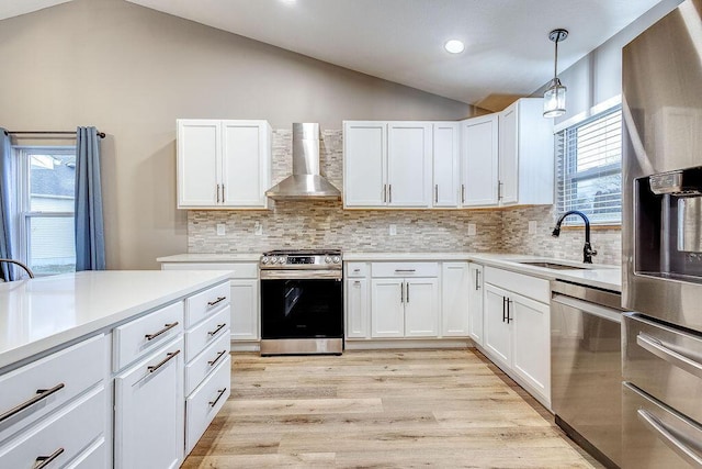 kitchen with stainless steel appliances, a sink, vaulted ceiling, light countertops, and wall chimney range hood