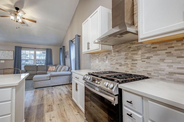 kitchen with light wood-style flooring, decorative backsplash, white cabinets, gas range, and wall chimney exhaust hood