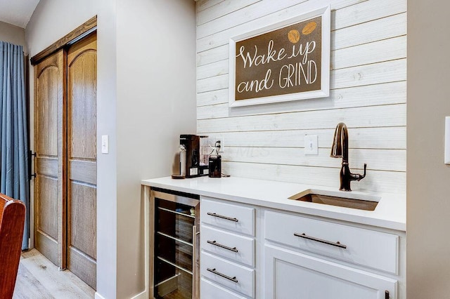 bar featuring wine cooler, wood walls, a sink, light wood-style floors, and wet bar