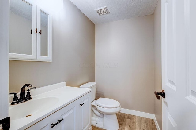 half bath featuring a textured ceiling, toilet, wood finished floors, vanity, and visible vents