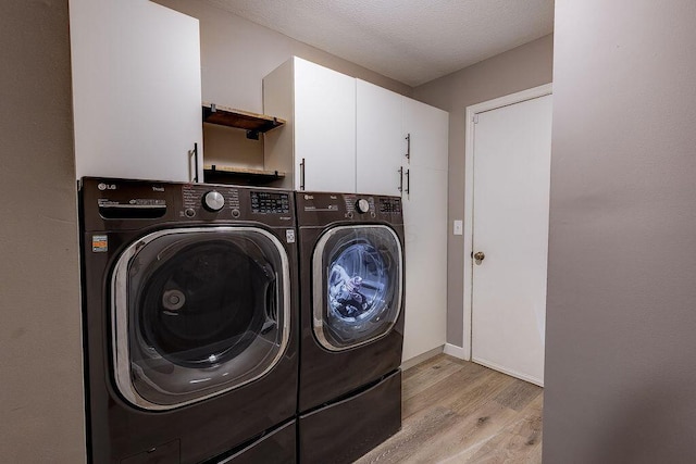 clothes washing area featuring a textured ceiling, light wood-style floors, baseboards, washer and dryer, and cabinet space