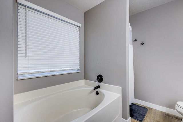 bathroom with baseboards, toilet, wood finished floors, a garden tub, and a textured ceiling