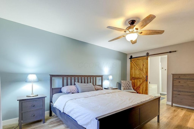 bedroom with light wood-style floors, a barn door, baseboards, and ceiling fan