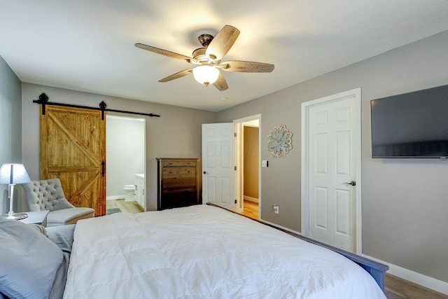 bedroom with ensuite bathroom, ceiling fan, a barn door, wood finished floors, and baseboards