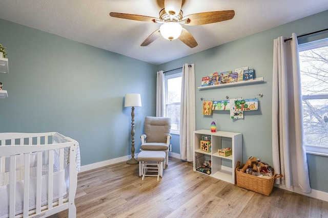 bedroom with a nursery area, multiple windows, and wood finished floors