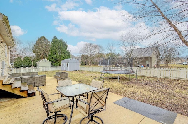 view of patio / terrace featuring a storage shed, a fenced backyard, an outbuilding, a trampoline, and outdoor dining space