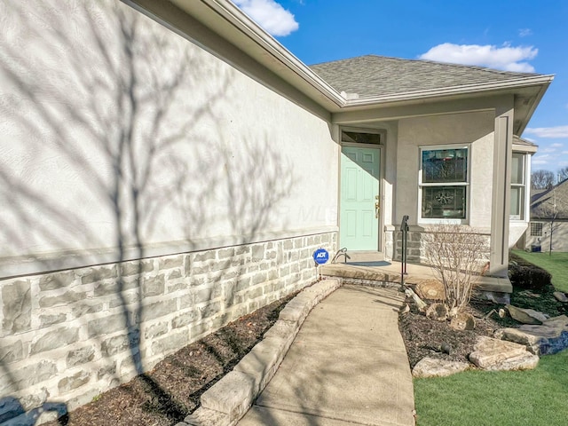 entrance to property with a shingled roof and stucco siding