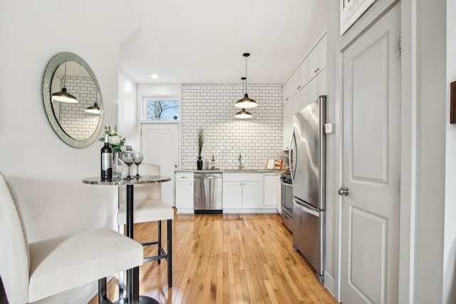 kitchen featuring light wood finished floors, decorative backsplash, stainless steel appliances, white cabinetry, and a sink