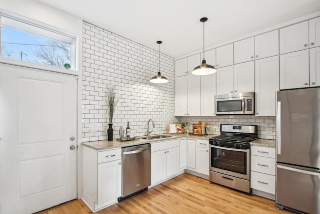 kitchen featuring tasteful backsplash, white cabinets, stainless steel appliances, light wood-type flooring, and a sink