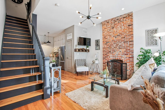 living area with a chandelier, a fireplace, visible vents, stairway, and light wood-type flooring