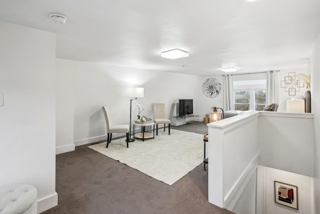 living area with dark colored carpet, an upstairs landing, and baseboards