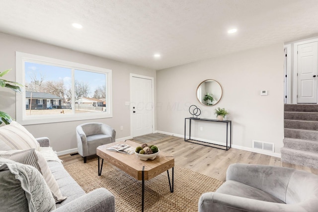 living room featuring light wood finished floors, stairway, visible vents, and baseboards