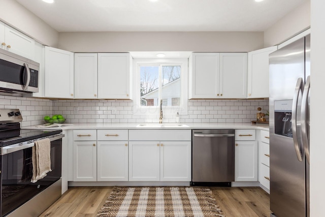 kitchen featuring tasteful backsplash, light wood-style flooring, appliances with stainless steel finishes, light countertops, and a sink