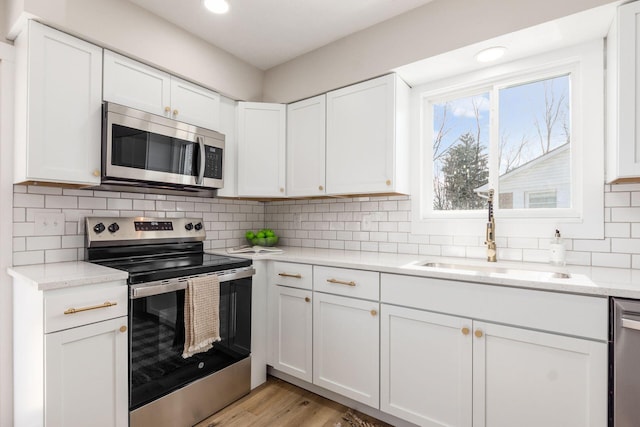 kitchen with backsplash, appliances with stainless steel finishes, white cabinetry, a sink, and light wood-type flooring