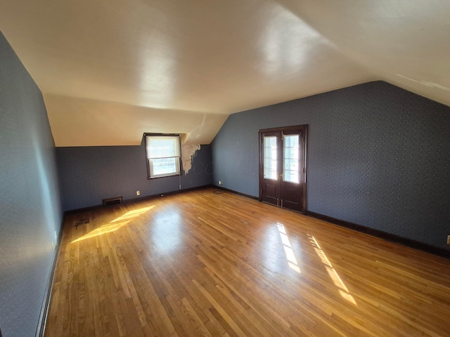 bonus room featuring wallpapered walls, visible vents, vaulted ceiling, and wood finished floors