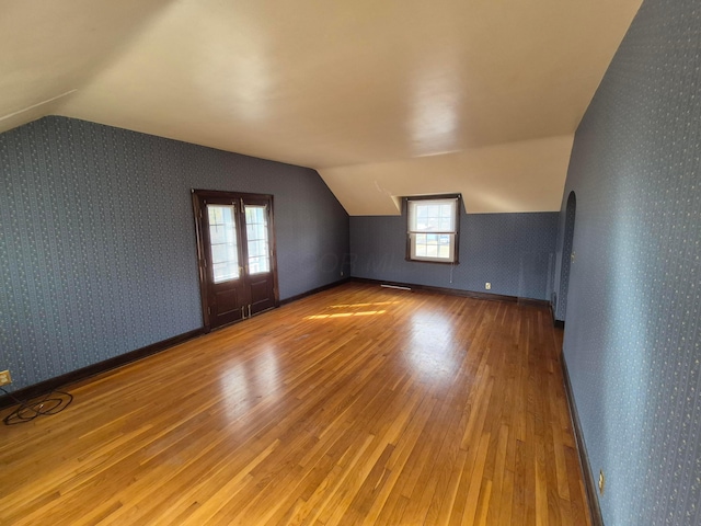 additional living space with vaulted ceiling, hardwood / wood-style flooring, and wallpapered walls