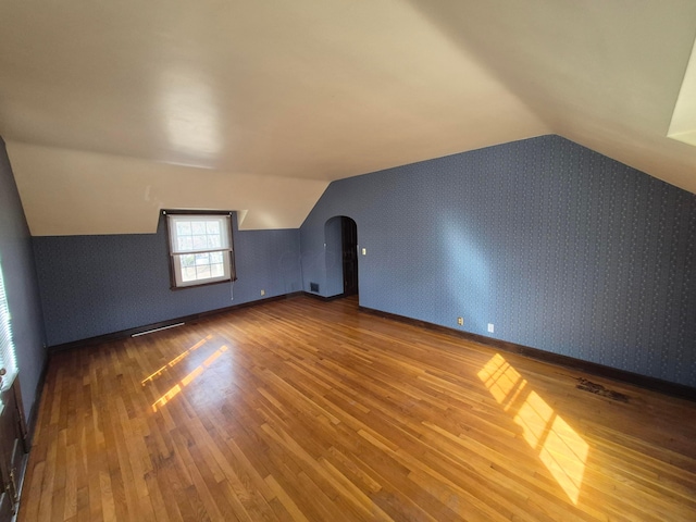 bonus room featuring arched walkways, lofted ceiling, wood finished floors, baseboards, and wallpapered walls