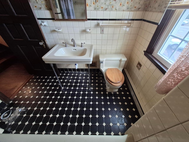 half bath with a sink, tile walls, toilet, and wallpapered walls