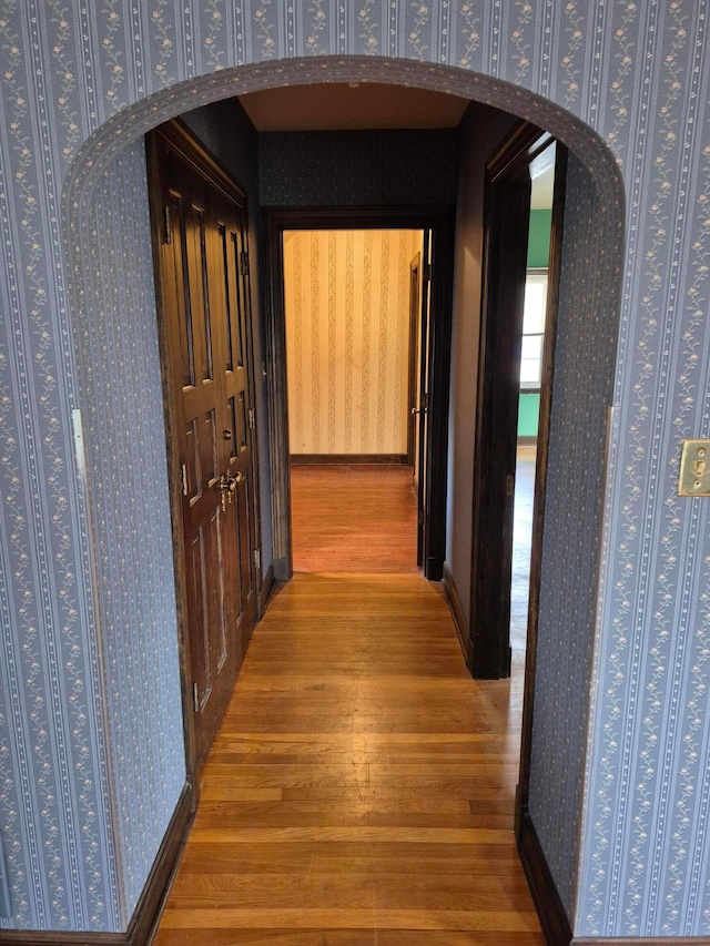 hall with arched walkways, wood finished floors, and wallpapered walls