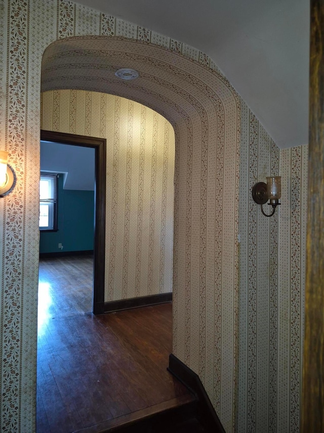 corridor featuring arched walkways, wood finished floors, lofted ceiling, and wallpapered walls