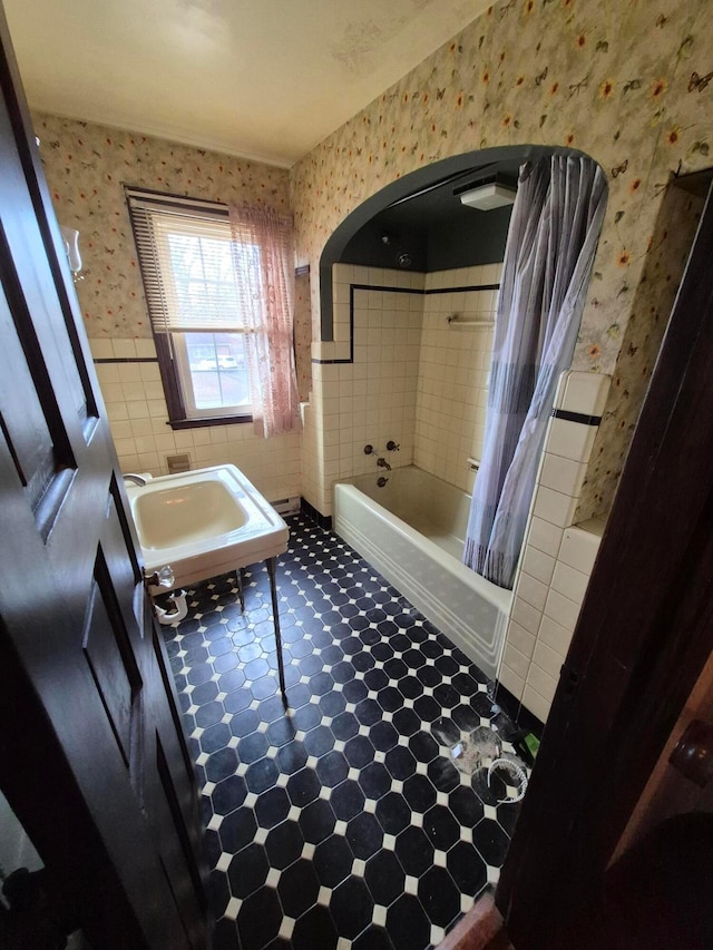 full bath with a sink, wallpapered walls, tile walls, and wainscoting