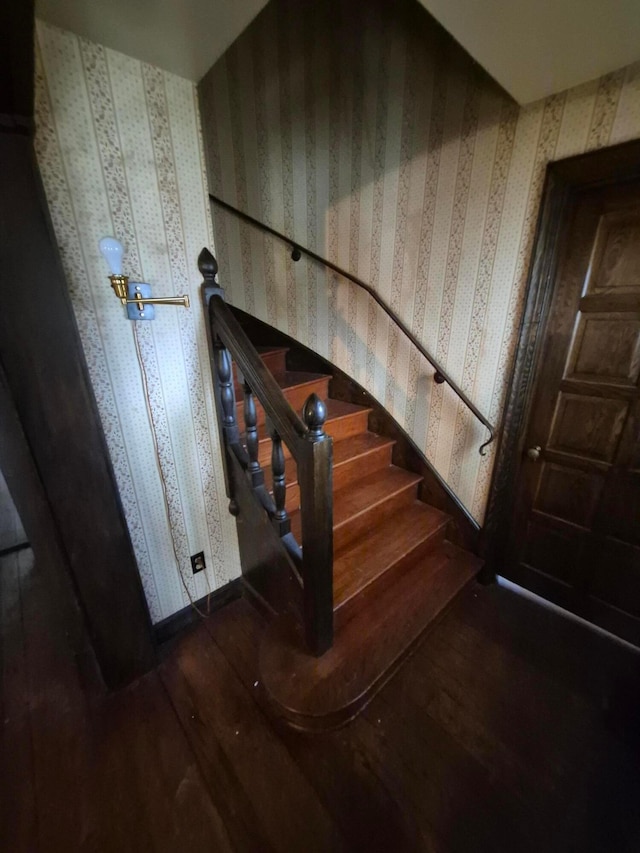 staircase with wood finished floors and wallpapered walls