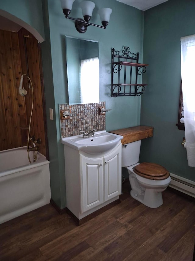 bathroom with toilet, wood finished floors, vanity, baseboard heating, and decorative backsplash