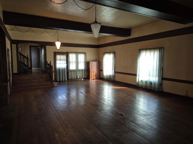 empty room featuring stairs, beamed ceiling, wood-type flooring, and a textured ceiling