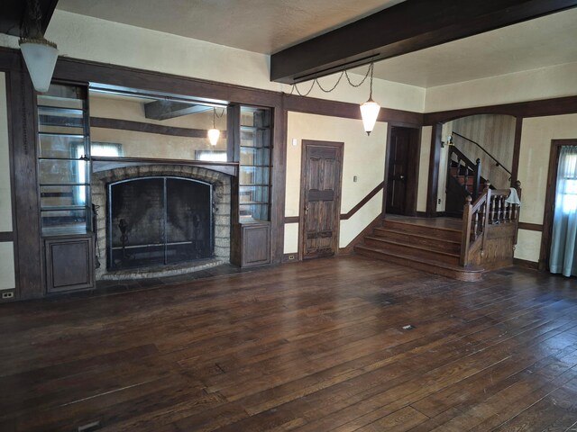 unfurnished living room with arched walkways, beam ceiling, wood-type flooring, a fireplace with raised hearth, and stairs