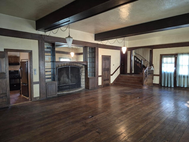 unfurnished living room featuring a fireplace with raised hearth, beamed ceiling, stairs, and hardwood / wood-style flooring