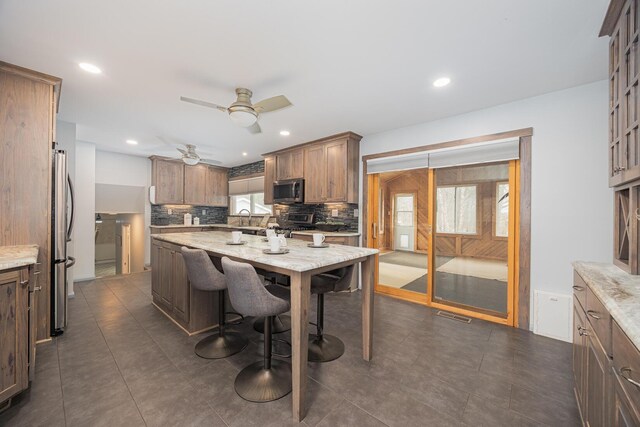 kitchen featuring light stone counters, tasteful backsplash, appliances with stainless steel finishes, a sink, and a kitchen bar