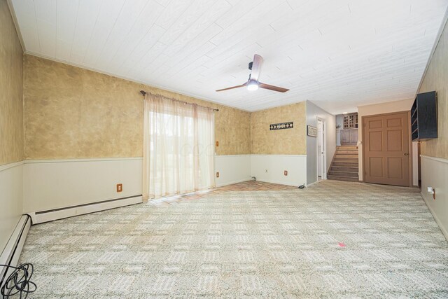 carpeted empty room with a wainscoted wall, stairway, baseboard heating, and a ceiling fan