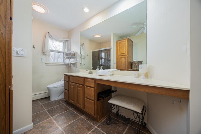 bathroom featuring toilet, a baseboard heating unit, vanity, baseboards, and stone tile flooring