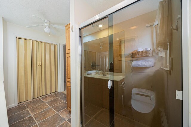 bathroom featuring a ceiling fan, stone finish flooring, an enclosed shower, a textured ceiling, and vanity