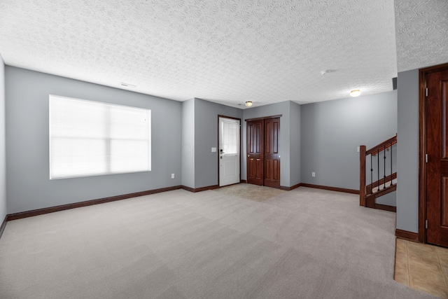 spare room with light carpet, stairway, a textured ceiling, and baseboards