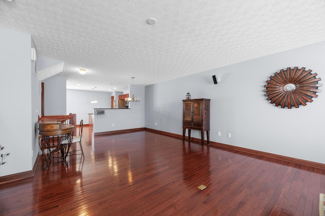unfurnished living room featuring an inviting chandelier, wood-type flooring, baseboards, and a textured ceiling