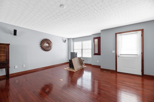 unfurnished living room with a textured ceiling, wood-type flooring, visible vents, and baseboards