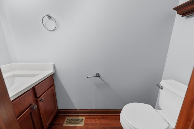 half bathroom with toilet, wood finished floors, vanity, visible vents, and baseboards