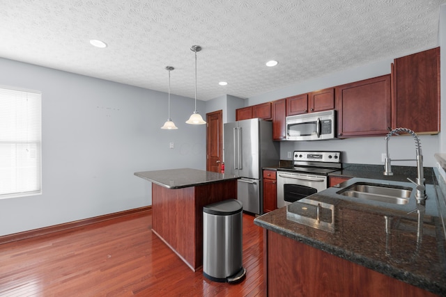kitchen featuring a center island, dark wood-style flooring, appliances with stainless steel finishes, a sink, and baseboards